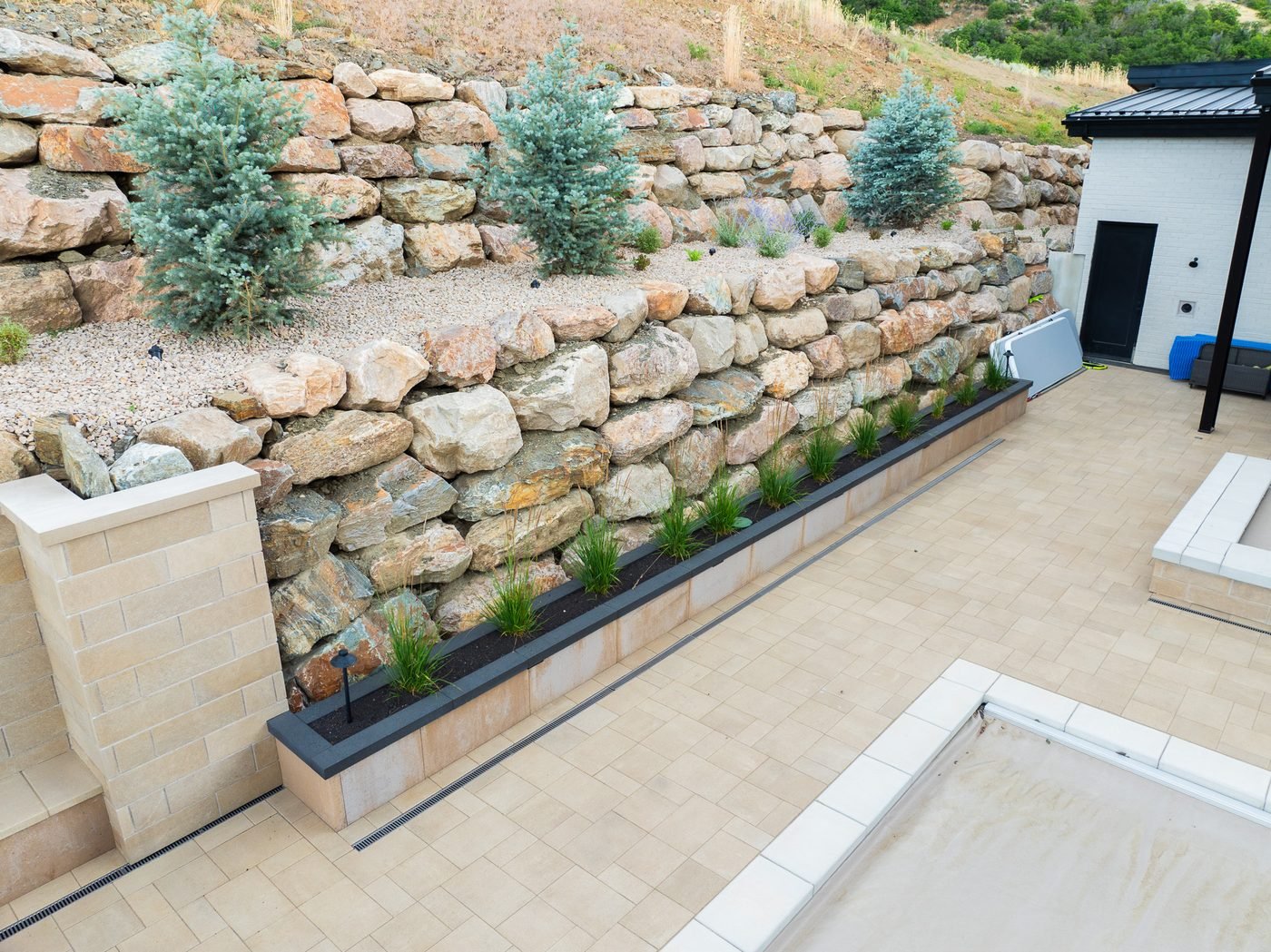 Paver deck with a trench drain, block seat wall and raised planter below tiered boulder walls