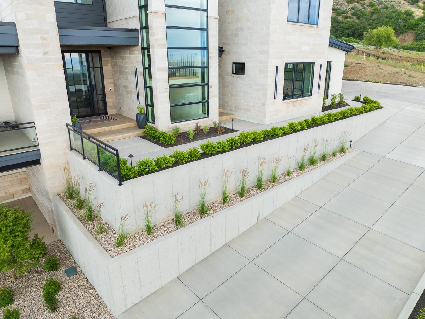 Board-formed concrete retaining walls holding a graded terrace beside a large-format paver driveway