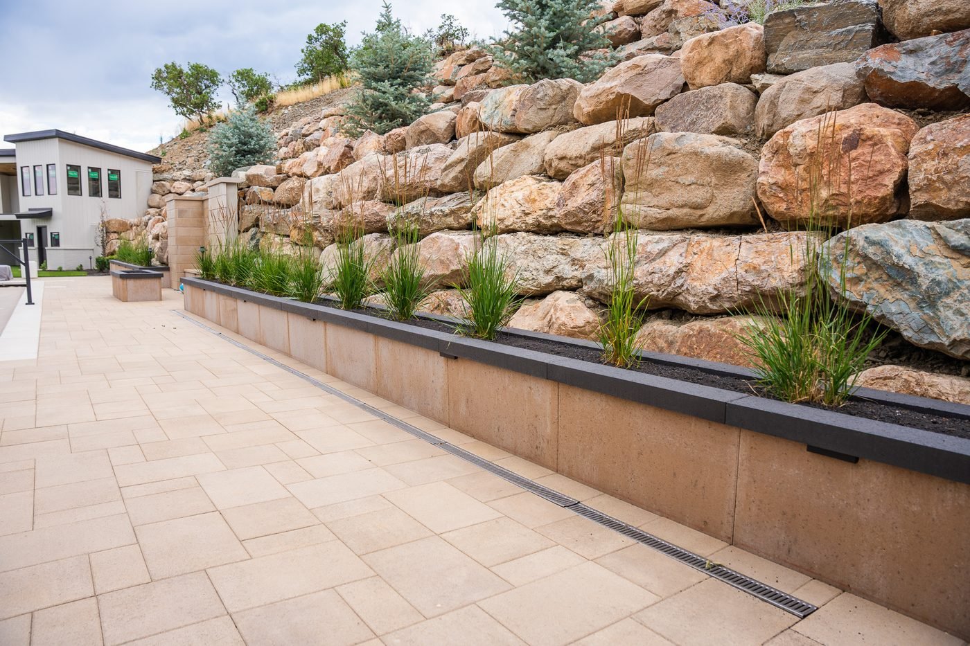 Large-format pavers laid in running bond beside a linear trench drain and a block seat wall with dark coping