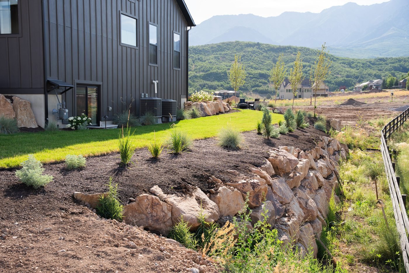 Boulder retaining wall holding a graded slope beside new sod and freshly planted beds