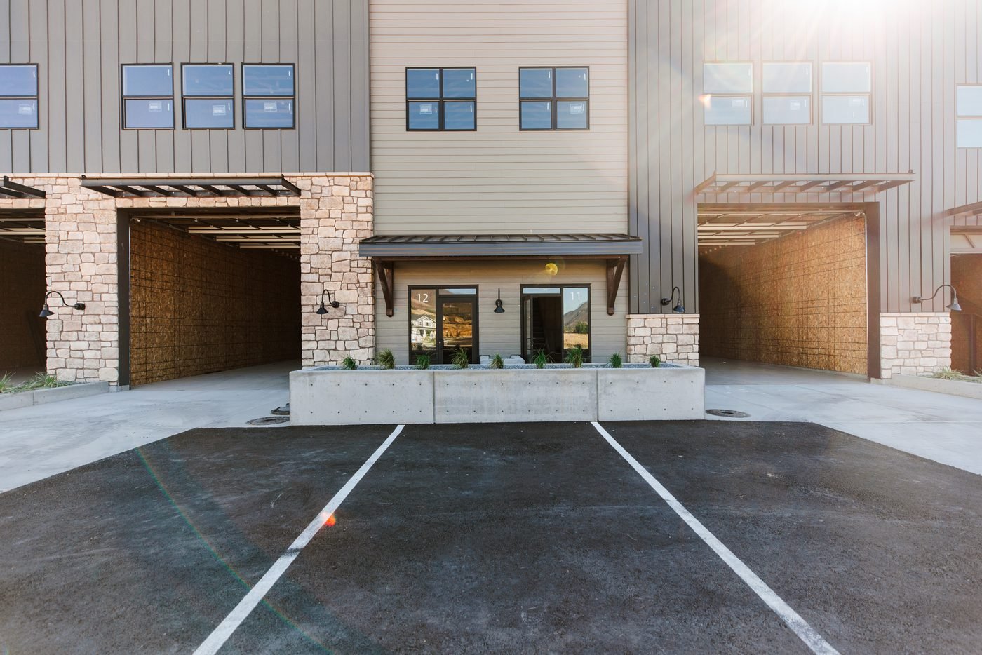 Cast concrete planters with ornamental grasses and gravel at a commercial building entry, beside a striped parking lot