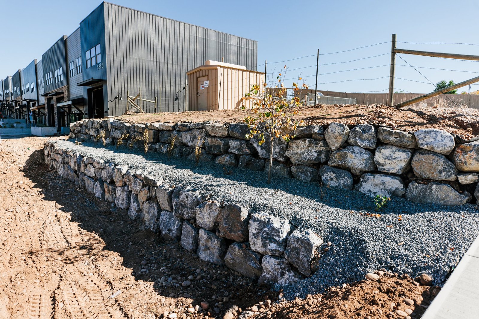 Two tiers of boulder retaining wall with clean drainage rock terraced between them, on a graded commercial site in Northern Utah
